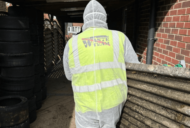 Man in The Waste Team branded high-vis jacket carrying asbestos waste from a building
