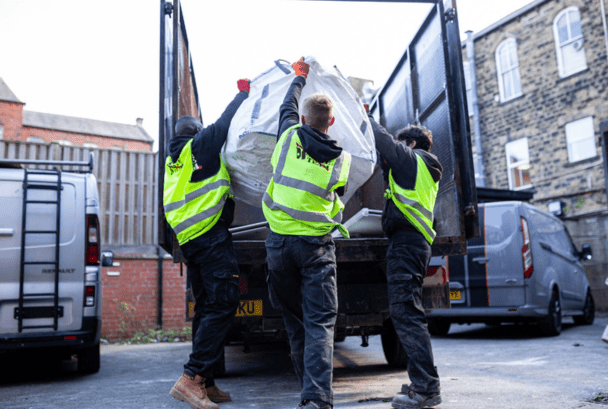 3 men lifting a commercial bag of building waste into the back of a large The Waste Team branded van