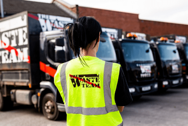 Women in The Waste Team branded high vis jacket stood in front of The Waste Team large waste removal vans