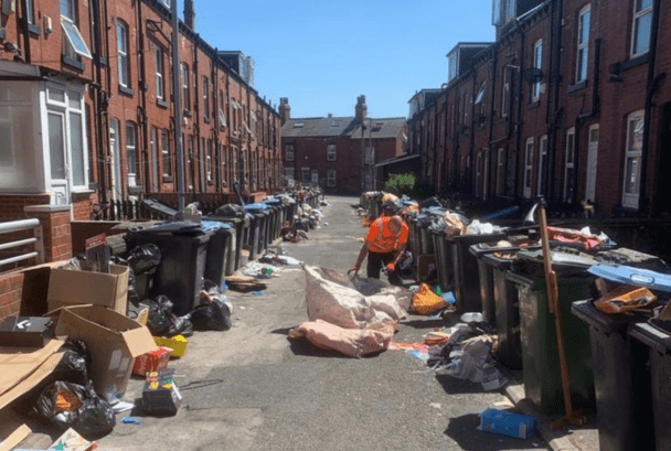 Row of terraced houses with overflowing bins and worker collecting rubbish