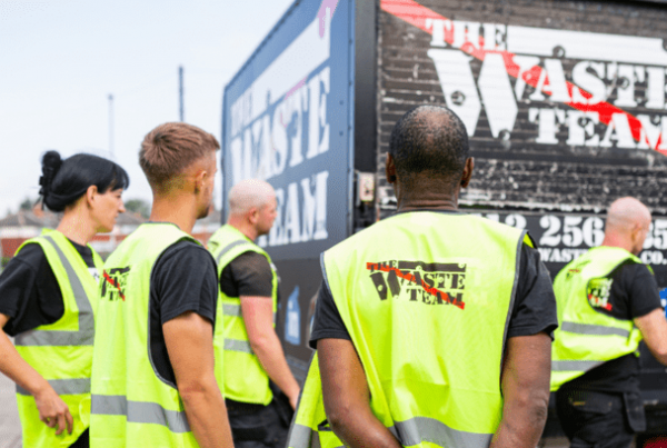 The Waste Team workers all wearing branded yellow high vis jackets facing away from the camera in a morning huddle by one of their vans