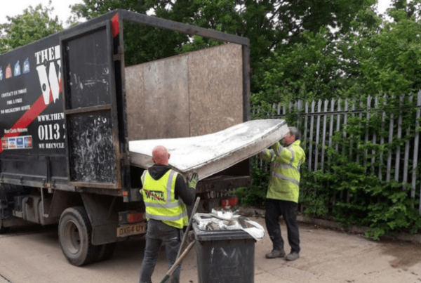 two men in high vis jackets putting an old mattress into the back of a The Waste Team branded van for recycling